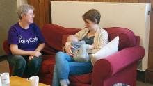 A Breastfeeding Counsellor and a Mother feeding her baby receiving support, sat on a couch together